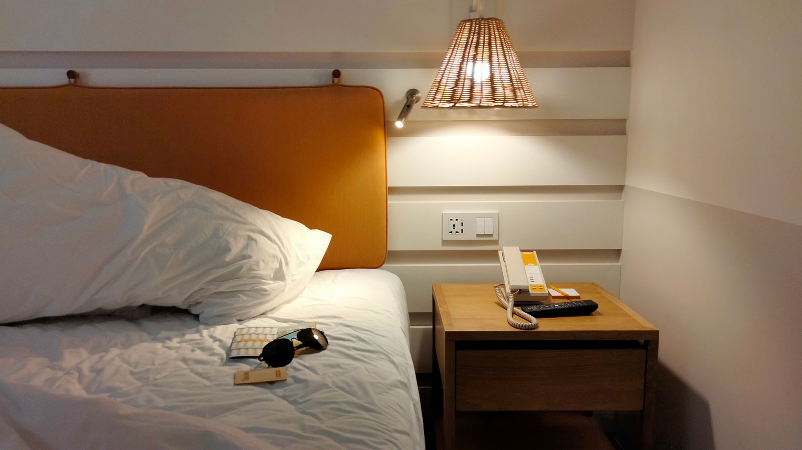 Hotellihuoneen sänky ja yöpöytä lampun valossa
